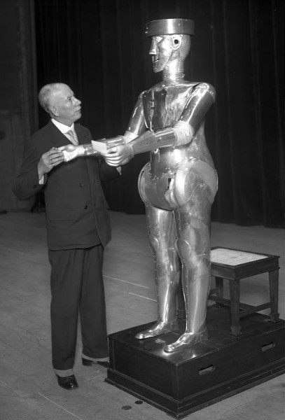 Old photo of an elderly gentleman looking up at a larger robot.